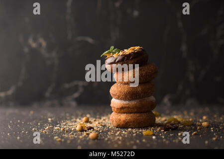 Stack of Donuts with crumbs, nuts and dried fruits on dark stone background Stock Photo