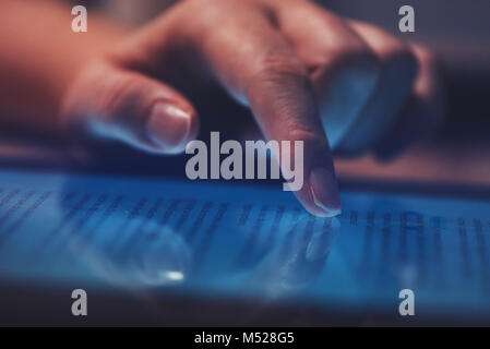 Extreme close up of female finger using digital tablet computer at home in the evening to read the news online, selective focus Stock Photo