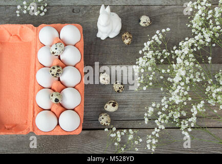 Orange carton box with white chiken and gual eggs and easter decor, bunny, white flower. Top view. Copy space. Stock Photo