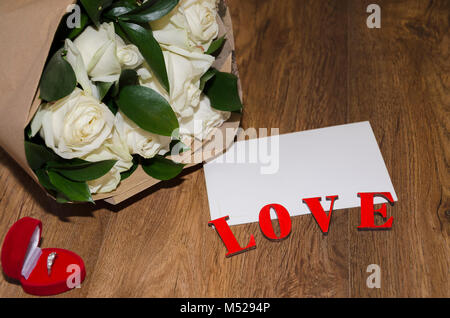 inscription love on a wooden background with a white sheet of paper and a bouquet of white roses in kraft paper Stock Photo
