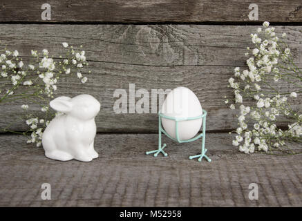 White porcelain rabbit and white chiken eggs on vintage wooden background. Easter's Background. Retro style postcard. Stock Photo