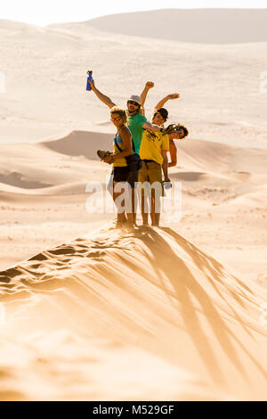 Group of friends standing in Namib Desert smiling and waving while looking at camera, Namibia Stock Photo