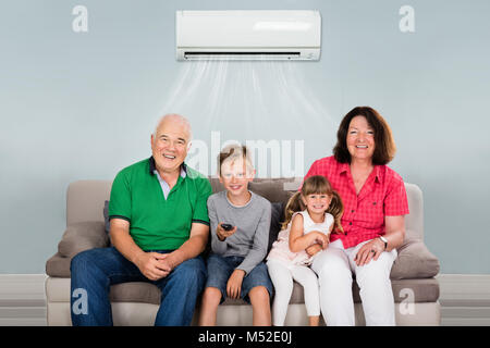 Happy Multi Generation Family With Two Kids Watching Television Under Air Conditioning At Home Stock Photo