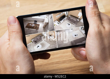Person's Hand Holding Smartphone And Monitoring Video Footage Against Wooden Table Stock Photo