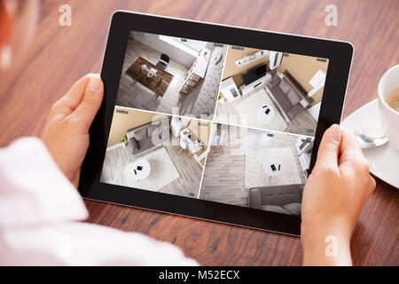 Elevated View Of A Person's Hand Looking At Home Security Cameras On Tablet Stock Photo