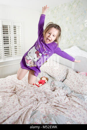 four year old girl jumping on parents bed Stock Photo