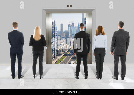 Rear View Of Businessman And Businesswoman Looking At Modern Elevator With Opened Door To City Stock Photo