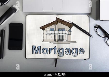 Drawing Of House And The Text Mortgage Shown In Book With Mobile Phone On Desk Stock Photo
