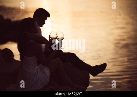 Romantic couple drinking wine at sunset at a pier on a seaside.Romance.Two people having a romantic evening with a glass of wine near the sea.Enjoying Stock Photo