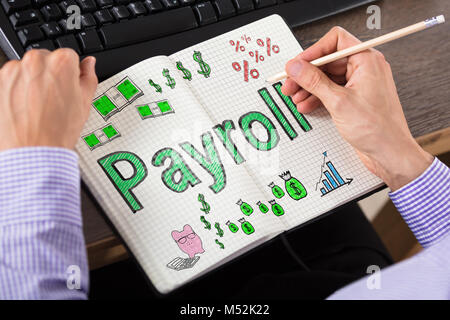 Close-up Of Person's Hand Writing Payroll In Book At Desk Stock Photo
