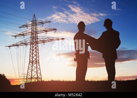 Silhouette Of Two Engineers Discussing Together With Electricity Pylon In Background Stock Photo