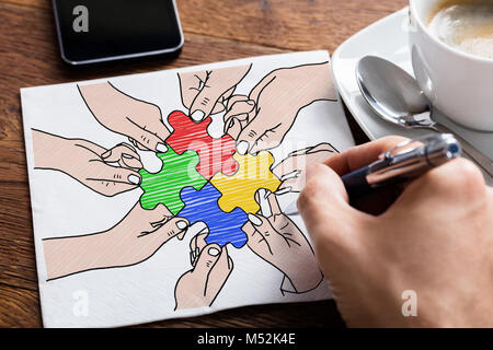 Close-up Of Person's Hand Drawing Colorful Jigsaw Puzzles On Paper On Desk Stock Photo