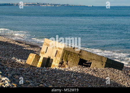 World War II defence concrete bunker sunk in shingle beach, Spey Bay, Moray, Scotland, UK, Lossiemouth in distance Stock Photo