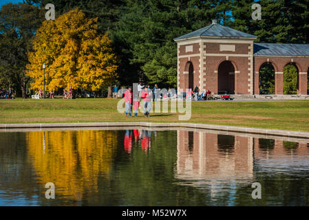 Family walk in the park past fall reflection on pool. Stock Photo