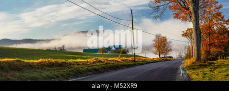 Landscape of morning mist rolling across a back road lined with Autumn's colourful red Maple leaves in Lisbon, NH, USA. Stock Photo