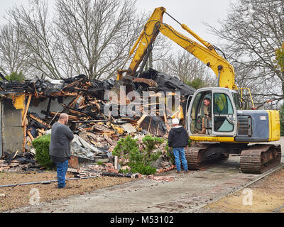 Workers using heavy duty excavator to help demolish a house that caught fire and burned in Montgomery Alabama, USA. Stock Photo