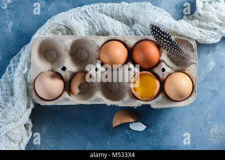 Brown eggs in craft carton pack with white runner and feathers on a concrete background. Fresh ingredients for Easter cooking. Top view with copy spac Stock Photo