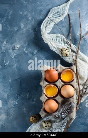 Hen and quail eggs in a carton with tree branches and cloth runner on a concrete background. Top view with copy space. Modern Easter concept Stock Photo