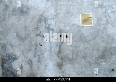 old grey concrete garage wall with spots of black paint with white ventilation grille abstract background Stock Photo