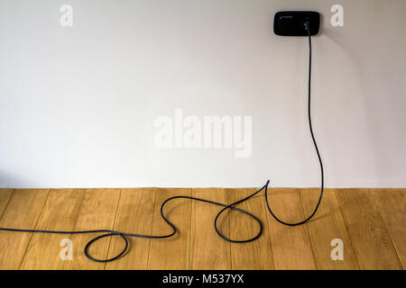 Black electric cable in wall socket on wooden parquet floor Stock Photo