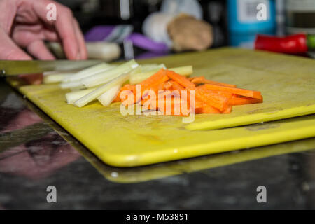 Authentic and candid shot of woman chopping celery next to batons of carrots in preparation for a stir fry. Stock Photo