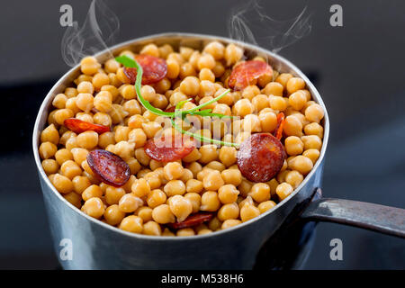 real homemade chickpeas, steaming stew with chorizo on a black background Stock Photo
