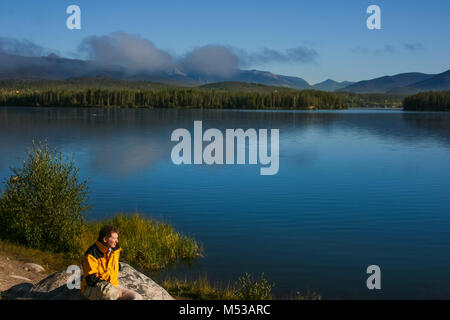 Mature man siting on the shore of Grand Lake, Colorado, enjoying the view of the lake covered with mist; summer Stock Photo