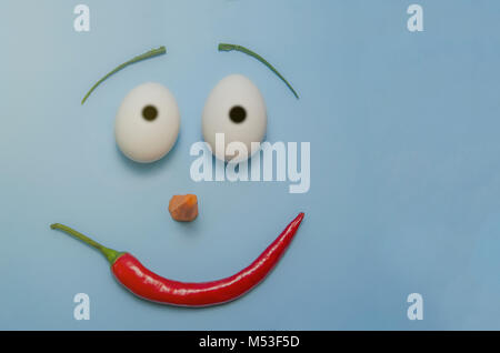 happy easter emoji from eggs, pepper, carrot and aloe on a blue background. Stock Photo