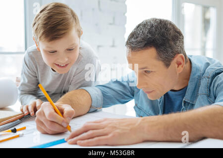 Cheerful boy watching his father sketch blueprint in office Stock Photo