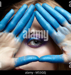 Eye of Providence, eye pyramid symbol made of hands and female face with blue paint on fingers Stock Photo