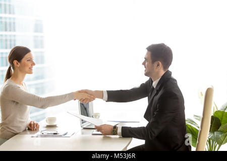 Businesswoman handshaking with businessman at desk Stock Photo