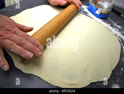 Hands roll the dough on the table with a rolling wooden pin Stock Photo