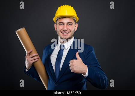 Male builder with helmet holds a tube with a work plan or blueprints for house construction Stock Photo