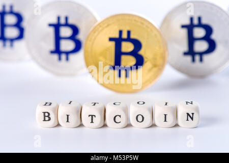 Single word BITCOIN made of wooden blocks with several golden and silver colored Bitcoin coins standing on white background, cryptocurrency concept Stock Photo