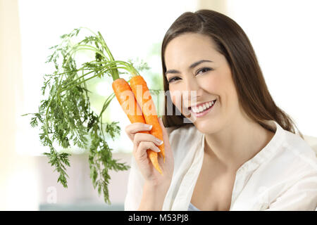 Portrait of a girl showing a bundle of carrots looking at camera sitting on a couch in the living room at home Stock Photo