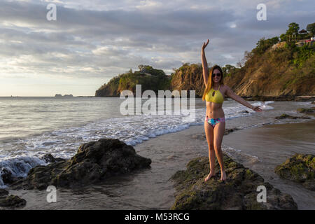 beautiful local latin model posing at the beach wearing a bikini with the sunset light on her in Playa Flamingo, Costa Rica Stock Photo