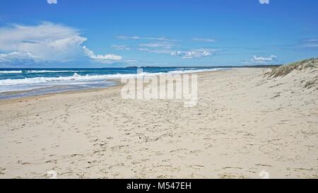 Footprint covered section of beach with ocean waves and blue sky in the background. Stock Photo