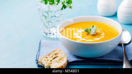 Pumpkin and carrot soup with cream and parsley on blue stone background. Copy space Stock Photo