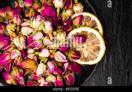 Rose tea buds and lemon slices on dark plate Stock Photo