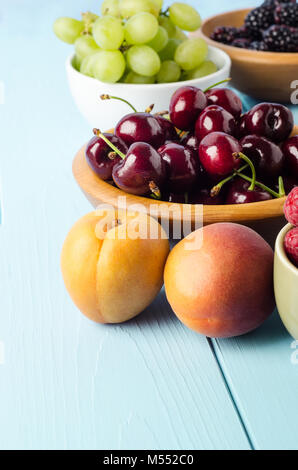 A variety of fruits, separated into wooden and ceramic bowls on light blue painted wood planked table. Stock Photo
