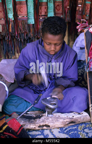 Algeria. Near Tamanrasset. Sahara desert. Boy of Tuareg tribe working iron. Blacksmith. Silversmith. Stock Photo