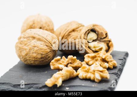 Several walnuts both in their shells and (un) shelled on black slate stone plate, whole setup isolated on white Stock Photo