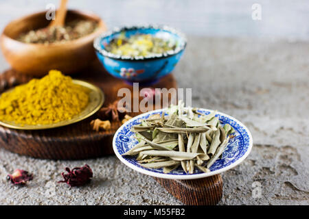 Dried olive leaves and dry spices in bowls on wooden Board on a concrete background Stock Photo