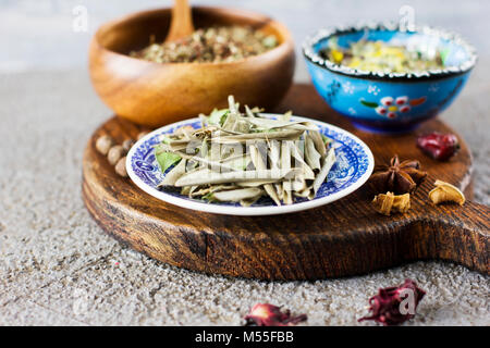 Dried olive leaves and dry spices in bowls on wooden Board on a concrete background Stock Photo