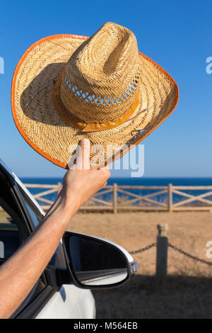 Arm in car holding straw hat at coast Stock Photo