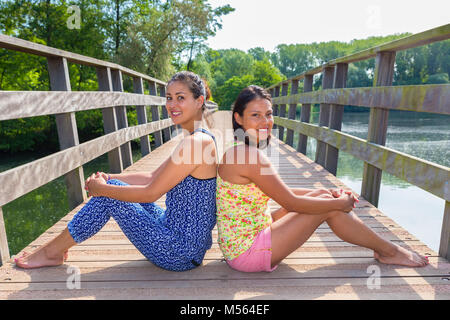 Two friends sit together on wooden bridge in nature Stock Photo