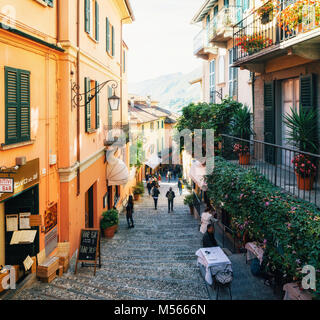 Bellagio, Italy - October 7, 2017: Tourists on narrow street with colorful houses in small town of Bellagio, Italy during sunny day. Como Lake Stock Photo