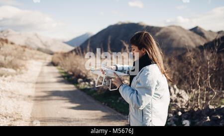 Young woman videographer catching flying aircraft with camera.Controlling landing of drone.Female filmmaker in nature using quad copter aircraft to ca Stock Photo