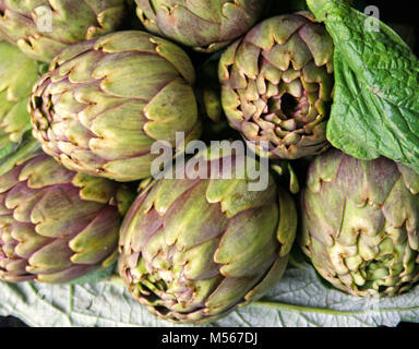 Beautiful fresh purple and green artichokes with green leaves on black background, close up Stock Photo