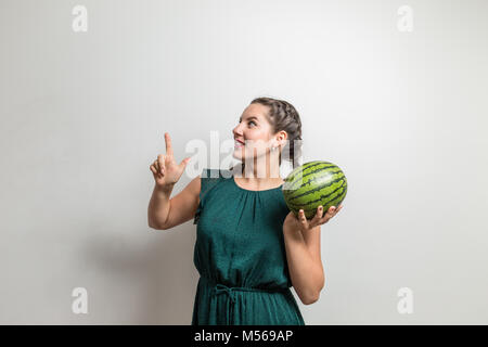 Portrait of a smiling pretty girl holding a watermelon and pointing finger to side isolated over white background Stock Photo